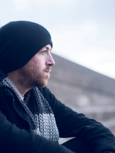 A young handsome man sitting alone by steps and contemplating life by the quiet sea, surrounded by raw concrete sea defence wall. Mental health and depression road to recovery.